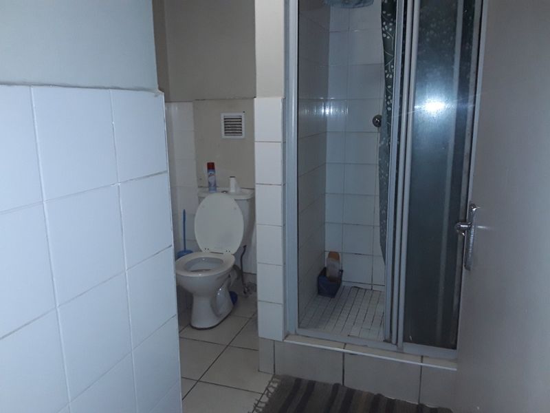 A functional bathroom featuring a shower enclosure, toilet, and tiled finishes throughout, presenting an opportunity for modernization and cosmetic updates.