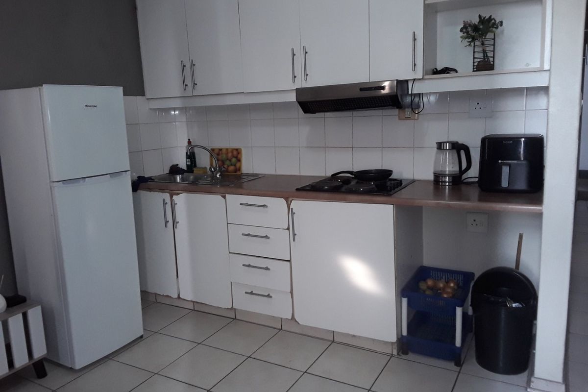 Compact kitchen featuring white cabinetry, tiled backsplash, built-in hob, and extractor fan with tiled flooring.