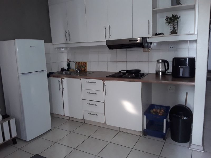 Compact kitchen featuring white cabinetry, tiled backsplash, built-in hob, and extractor fan with tiled flooring.