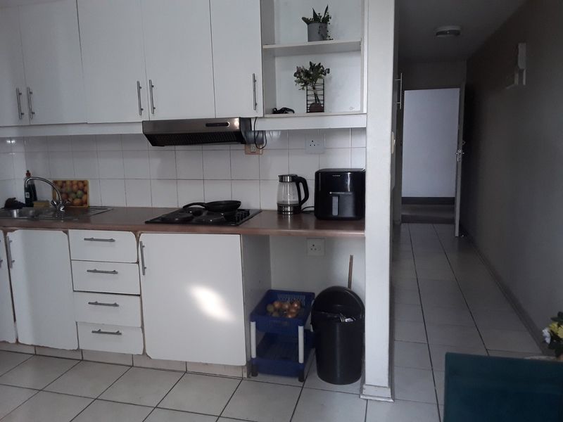 A functional kitchen featuring white cabinetry, a gas hob with extractor fan, laminate countertops, and tiled flooring, leading into a hallway.