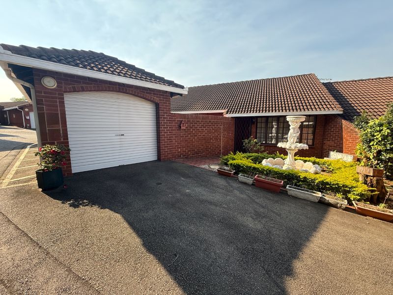 Front exterior view of the townhouse featuring a brick facade, tiled roof, and a private garage with a paved driveway.
