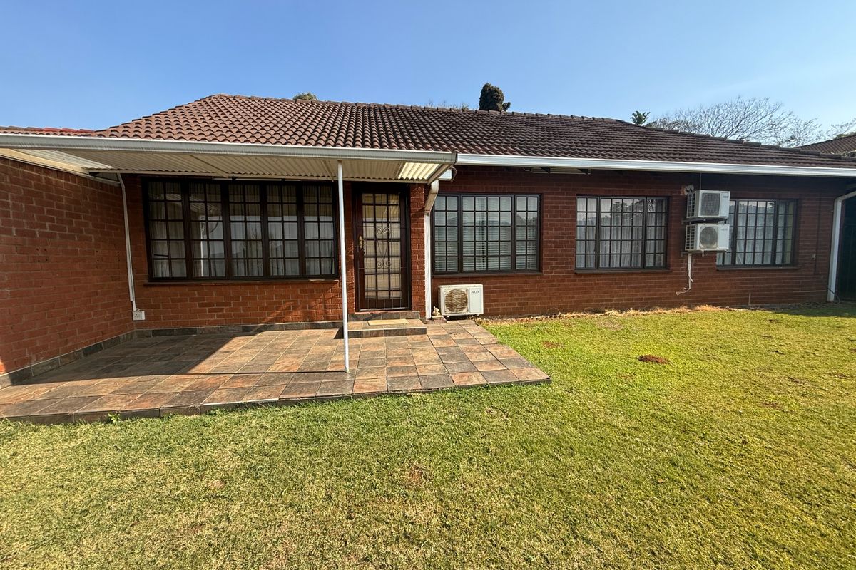 Rear view of the townhouse featuring a covered tiled patio, brick exterior, and established lawn area with multiple wall-mounted air conditioning units.