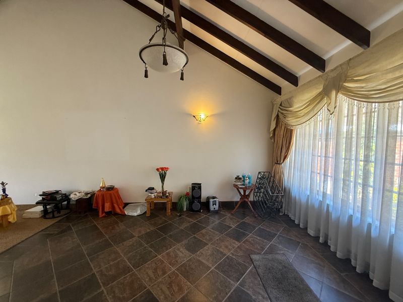 Spacious living area featuring vaulted ceilings with exposed timber beams, tiled flooring, and large windows allowing for ample natural light.