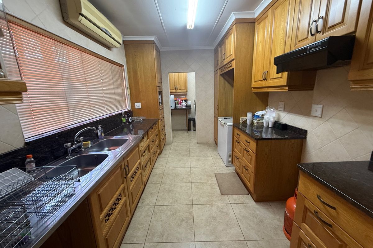 A functional kitchen featuring traditional wooden cabinetry, granite countertops, a double sink, and a tiled backsplash, with an adjacent scullery area.