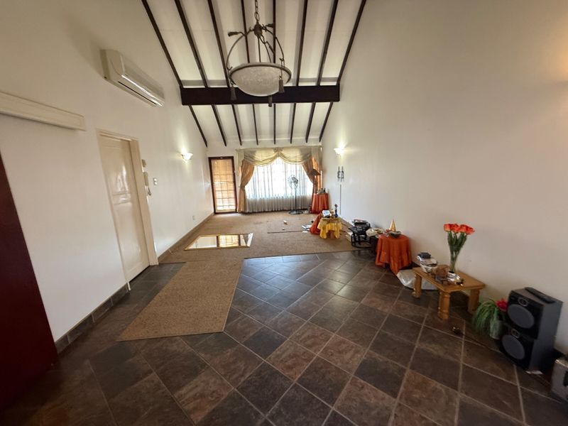 Spacious living area featuring vaulted ceilings with exposed timber beams, split-system air conditioning, and a combination of tiled and carpeted flooring.