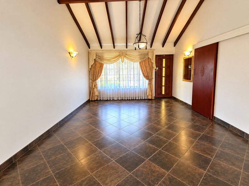 Spacious living area featuring exposed timber ceiling beams, dark tiled flooring, and a sliding door leading to the exterior.