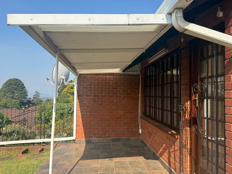 A covered outdoor patio area featuring tiled flooring, brick walls, and a metal roof structure, offering a functional space for outdoor relaxation.