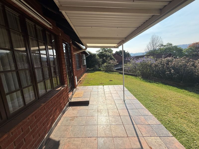 A covered outdoor patio area featuring tiled flooring and direct access to the rear garden, providing a functional space for outdoor relaxation.