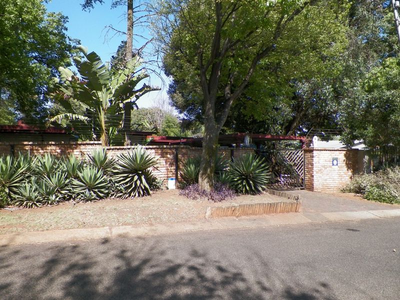 Front view of the property featuring a brick boundary wall, mature landscaping, and a secure metal gate entrance from the street.