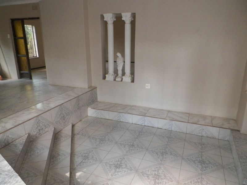 An empty living area featuring a sunken floor design, tiled flooring throughout, and a decorative wall niche with integrated columns.