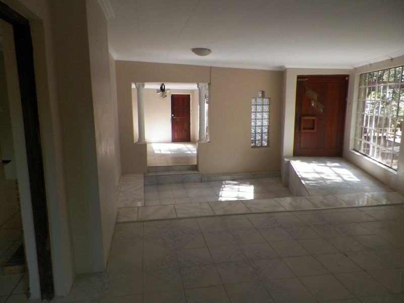 Spacious entrance hall featuring a raised platform, decorative columns, and a timber front door with natural light from a glass block window.