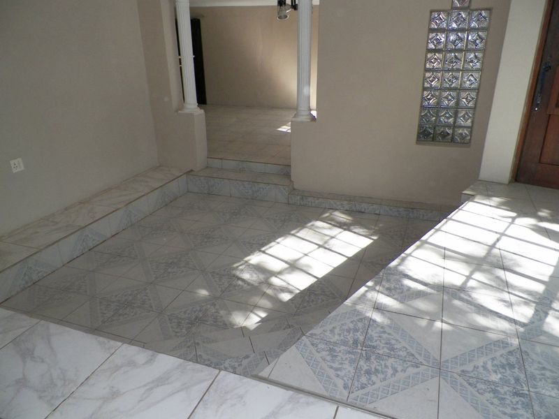 An empty living area featuring multi-level tiled flooring, decorative columns, and a glass block feature wall, offering a versatile space for renovation.