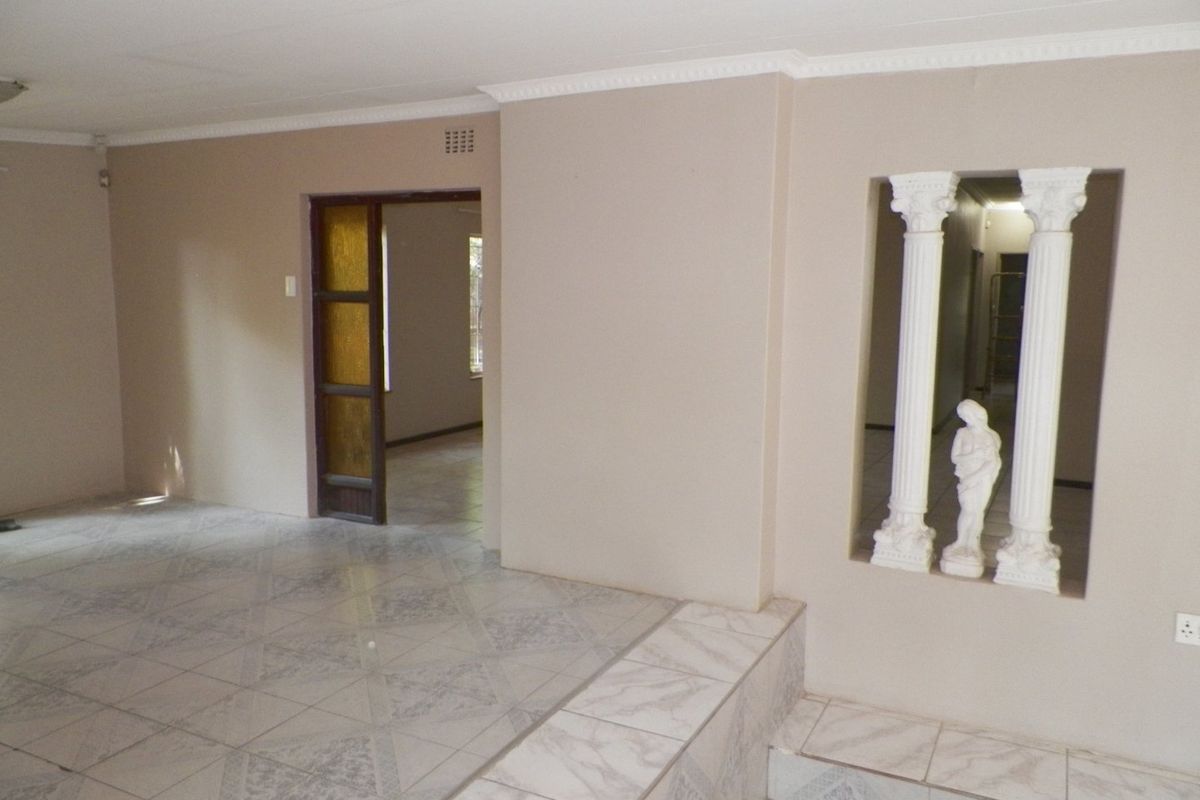An empty living area featuring tiled flooring, decorative columns, and coved ceiling details, offering a blank canvas for potential interior design updates.