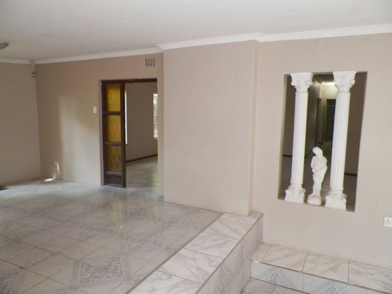 An empty living area featuring tiled flooring, decorative columns, and coved ceiling details, offering a blank canvas for potential interior design updates.