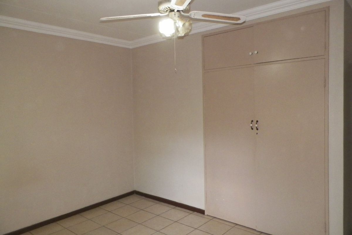An empty bedroom featuring tiled flooring, a ceiling fan, and built-in cupboards with neutral wall finishes.
