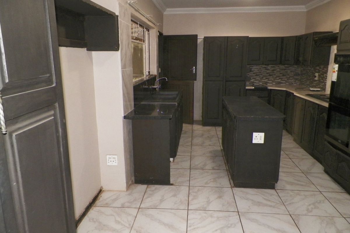 A spacious kitchen featuring dark built-in cabinetry, a central island, stone countertops, tiled flooring, and a built-in oven, offering a functional layout.