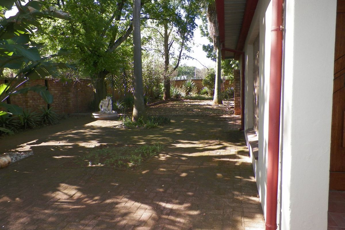A rear garden area featuring brick paving, mature trees, and a brick boundary wall, adjacent to the side of the house.