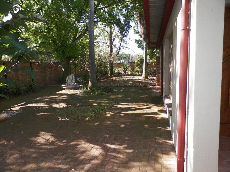 A rear garden area featuring brick paving, mature trees, and a brick boundary wall, adjacent to the side of the house.