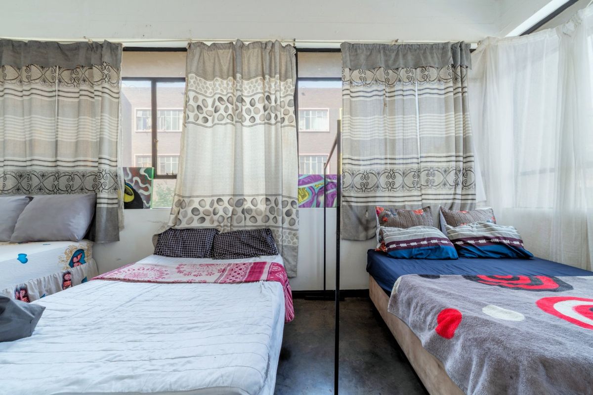 A bedroom featuring large windows with natural light and concrete flooring, offering a functional space with potential for modernization.