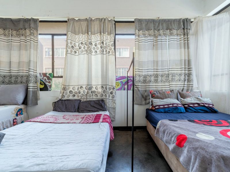 A bedroom featuring large windows with natural light and concrete flooring, offering a functional space with potential for modernization.