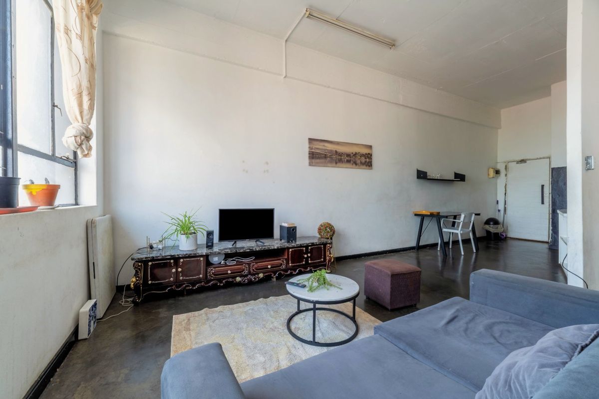Spacious living area featuring industrial-style concrete flooring, high ceilings with exposed beams, and large windows providing ample natural light.