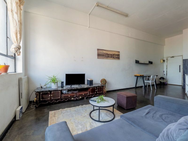 Spacious living area featuring industrial-style concrete flooring, high ceilings with exposed beams, and large windows providing ample natural light.