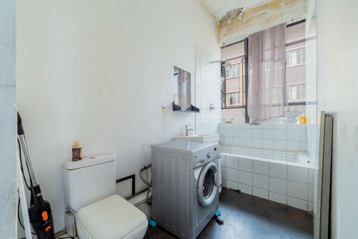 A bathroom requiring renovation, featuring a tiled bathtub, wall-mounted basin, and toilet, with visible ceiling and wall damage needing repair.