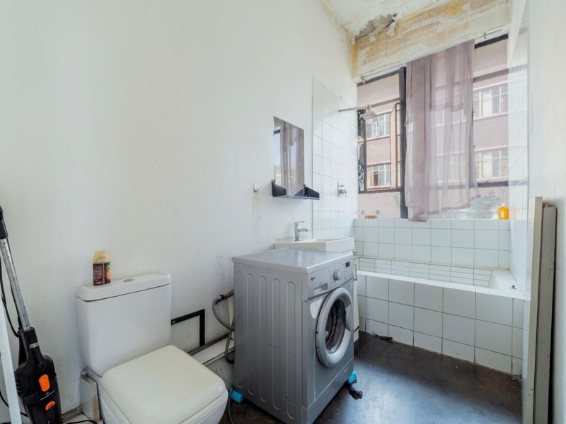 A bathroom requiring renovation, featuring a tiled bathtub, wall-mounted basin, and toilet, with visible ceiling and wall damage needing repair.