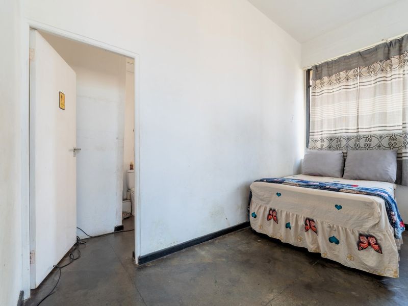 A bedroom featuring tiled flooring and direct access to an en-suite bathroom, requiring cosmetic updates to the wall finishes.