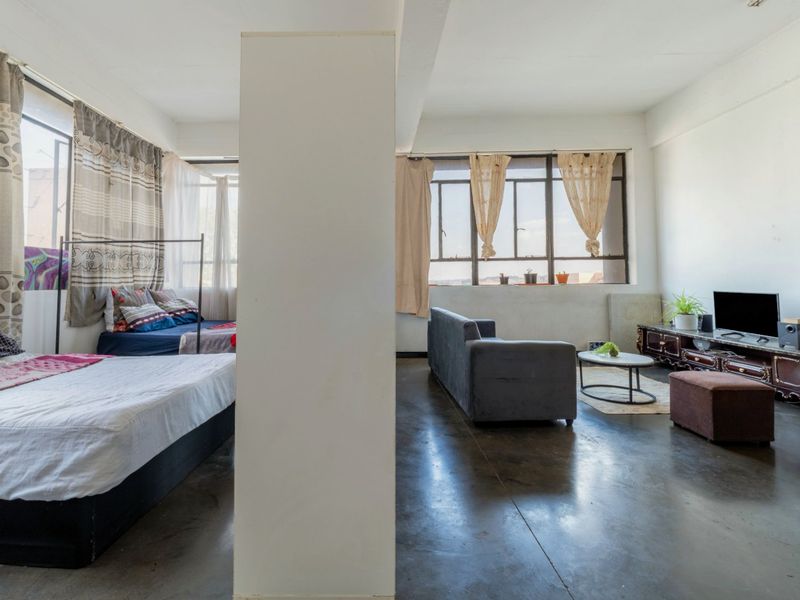 Open-plan living and sleeping area featuring polished concrete floors, large windows providing natural light, and a central structural column.
