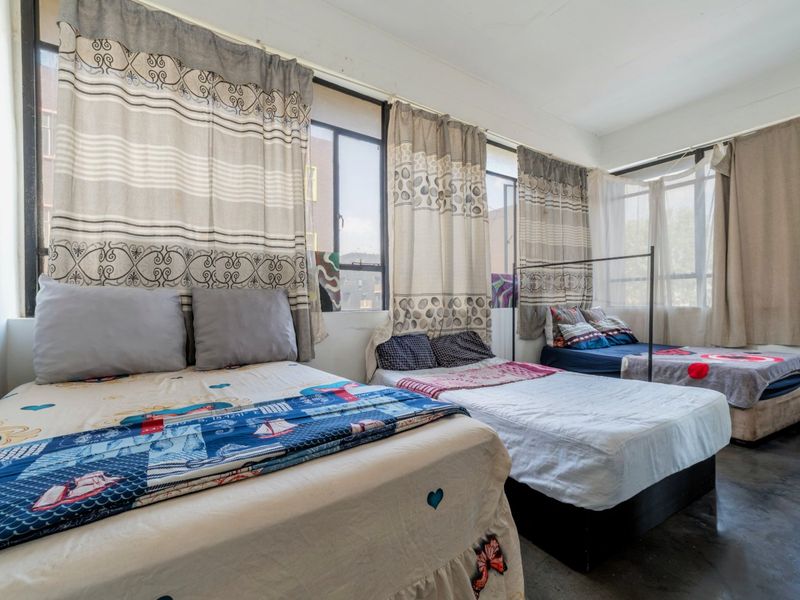 Spacious bedroom featuring large windows that provide ample natural light and durable concrete flooring, offering a functional space with potential for modernization.