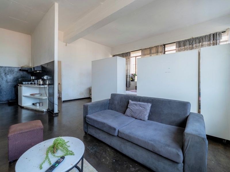 Open plan living area featuring a compact kitchen corner, concrete flooring, and built-in partition walls creating distinct functional zones.