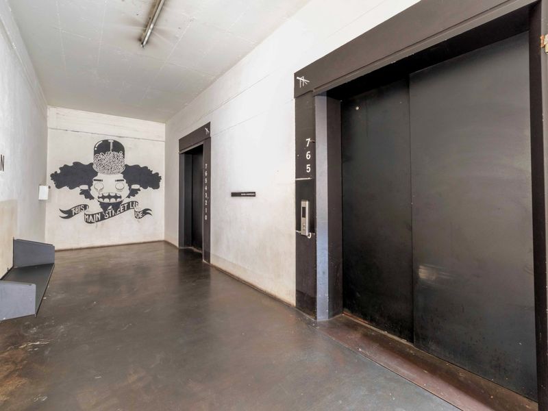 A utilitarian apartment building hallway featuring elevator access, concrete flooring, and industrial-style finishes with visible wear on the walls and floor.
