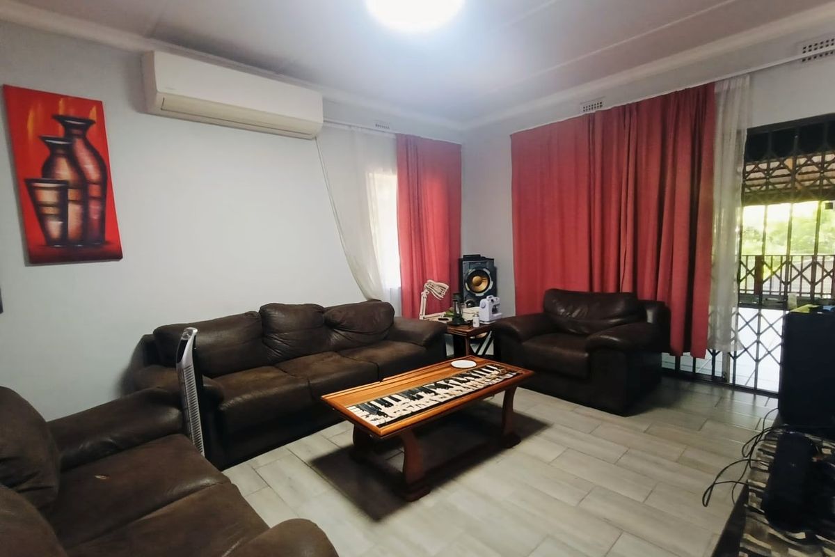 A comfortable living room featuring tiled flooring, a wall-mounted split-system air conditioner, and access to an outdoor area through a security gate.