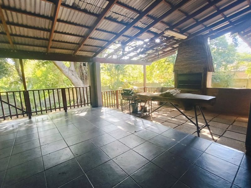 Covered outdoor patio featuring a built-in braai, tiled flooring, and timber balustrade, offering a spacious area for outdoor entertaining.