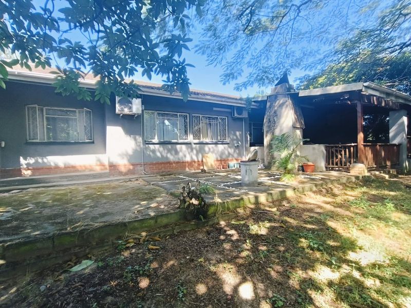 Rear exterior view featuring a concrete patio, built-in fireplace, and covered outdoor area, showing signs of wear and requiring maintenance.