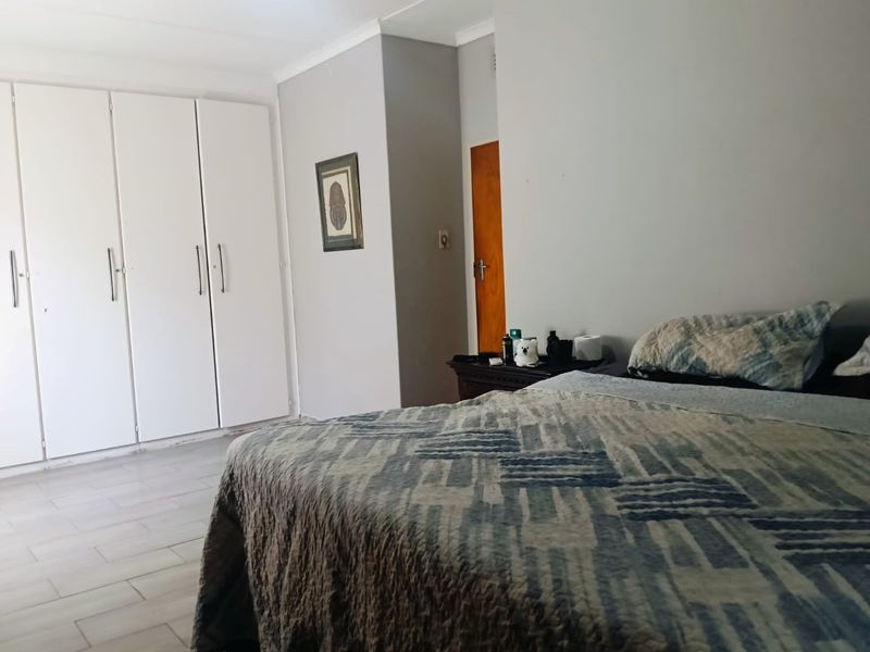 A bedroom featuring built-in cupboards, tiled flooring, and a wooden door, offering a functional and neutral living space.