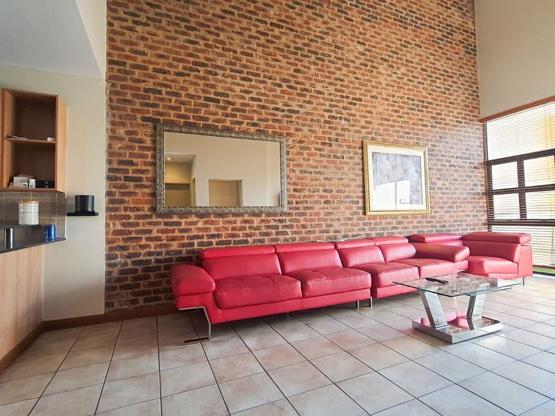 Spacious open-plan living area featuring a striking exposed brick wall, high ceilings, tiled floors, and an integrated kitchen with granite countertops.