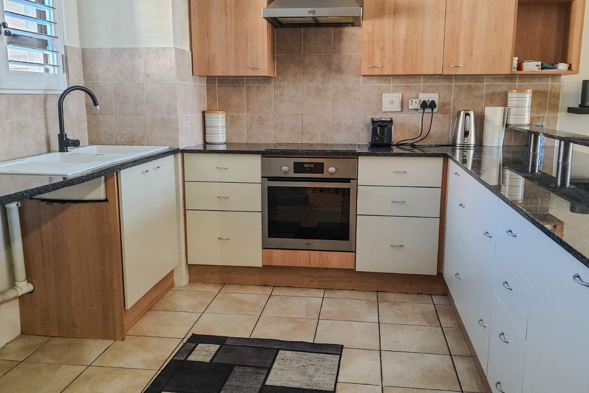 A functional kitchen featuring light wood and white cabinetry, granite countertops, a built-in oven, extractor fan, and tiled finishes throughout.