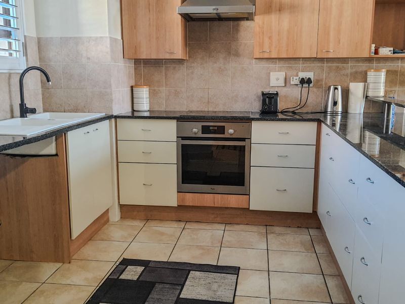 A functional kitchen featuring light wood and white cabinetry, granite countertops, a built-in oven, extractor fan, and tiled finishes throughout.