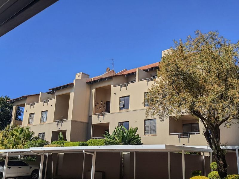 Exterior view of a multi-story apartment complex featuring a tiled roof, private balconies, and covered carport parking facilities.