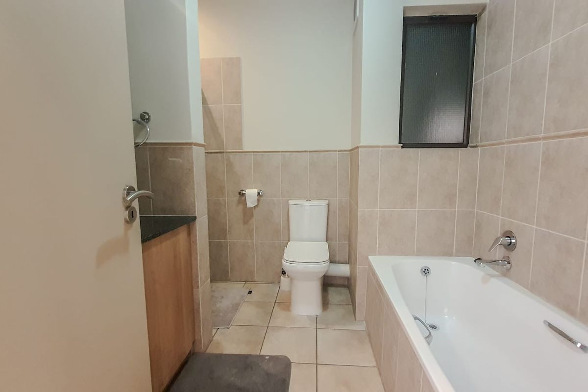 A functional bathroom featuring a built-in vanity with granite countertop, a standard toilet, and a bathtub with tiled wall finishes.
