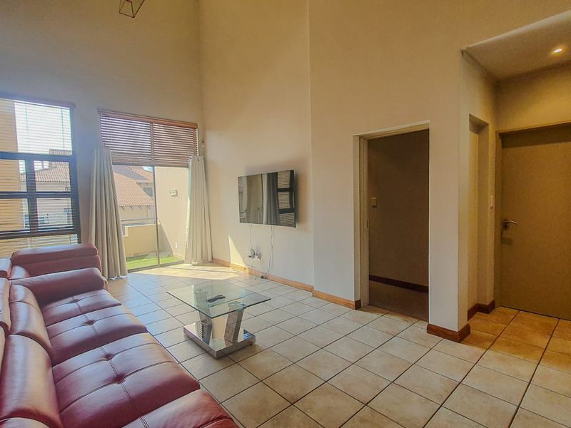 Spacious living room featuring high vaulted ceilings, tiled flooring, an exposed brick feature wall, and direct access to an outdoor patio area.