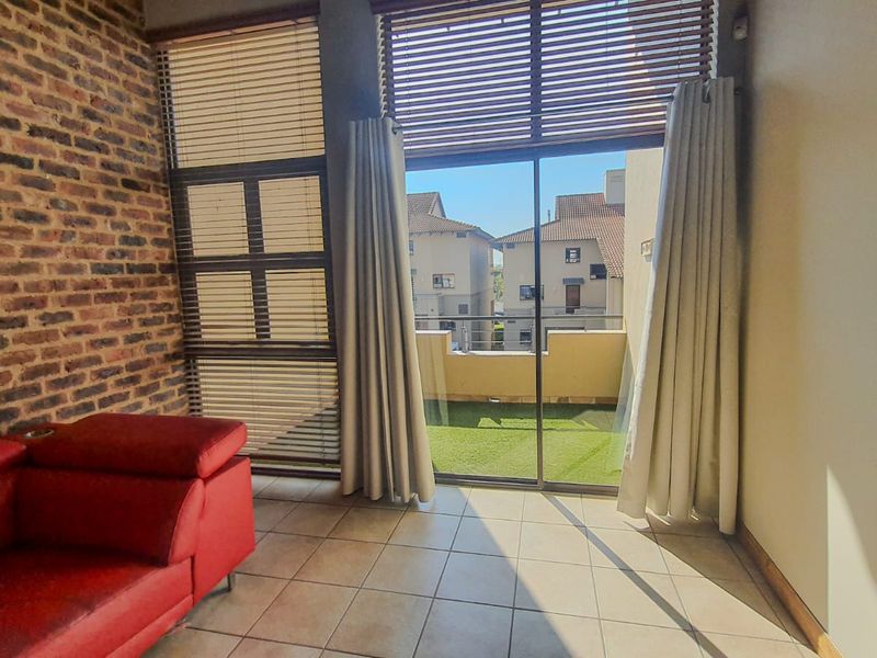 A bright living room featuring an exposed brick feature wall, tiled flooring, and large sliding glass doors leading to a private balcony.