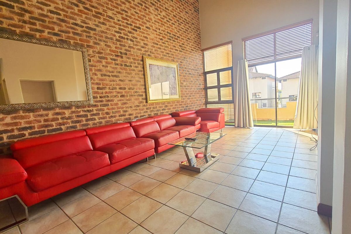 Spacious living room featuring a striking exposed brick feature wall, large format floor tiles, and expansive glass sliding doors leading to an outdoor area.