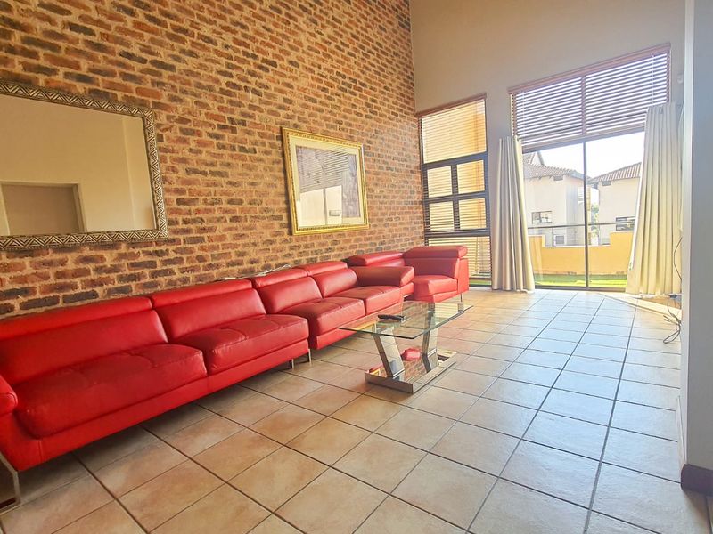 Spacious living room featuring a striking exposed brick feature wall, large format floor tiles, and expansive glass sliding doors leading to an outdoor area.