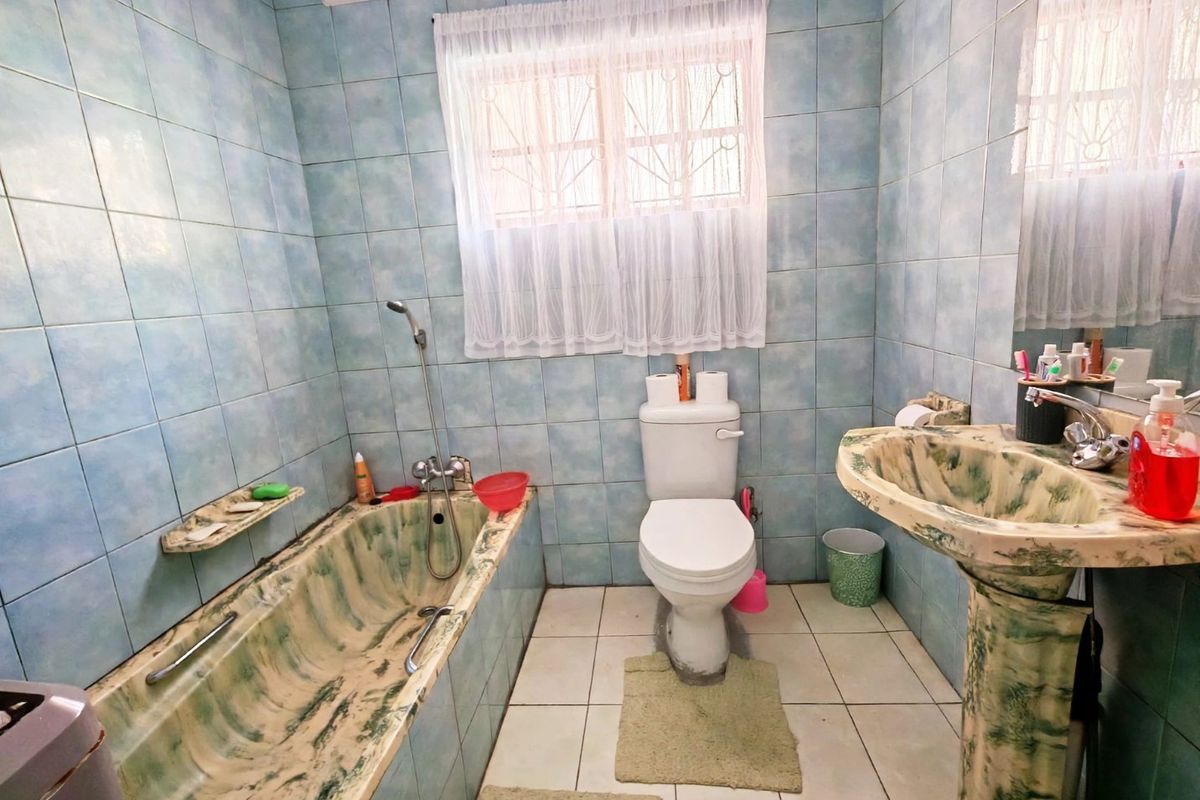 A dated bathroom featuring a built-in bathtub, pedestal basin, and toilet with blue wall tiles and white floor tiles.