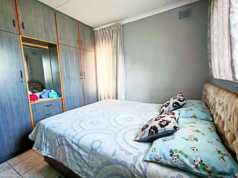 A bedroom featuring built-in cupboards with a mirrored vanity section and tiled flooring.