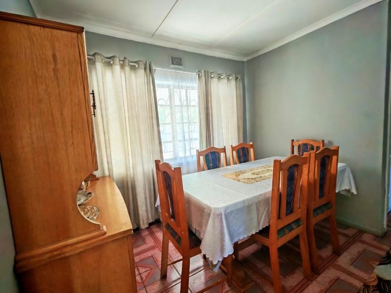 A functional dining room featuring tiled flooring, a window with security bars, and neutral wall finishes, offering a practical space for family meals.