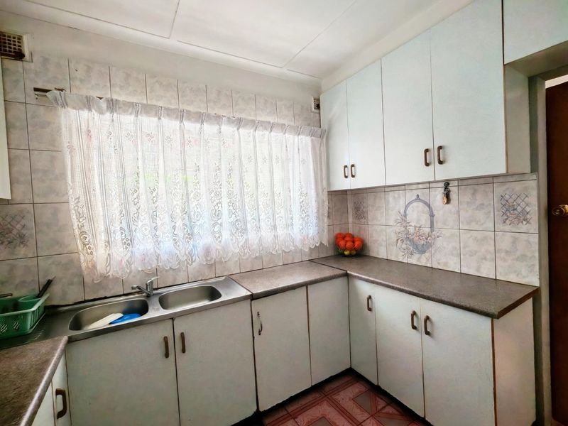 A functional kitchen featuring double bowl stainless steel sink, laminate countertops, and ample built-in cabinetry with tiled splashbacks and flooring.